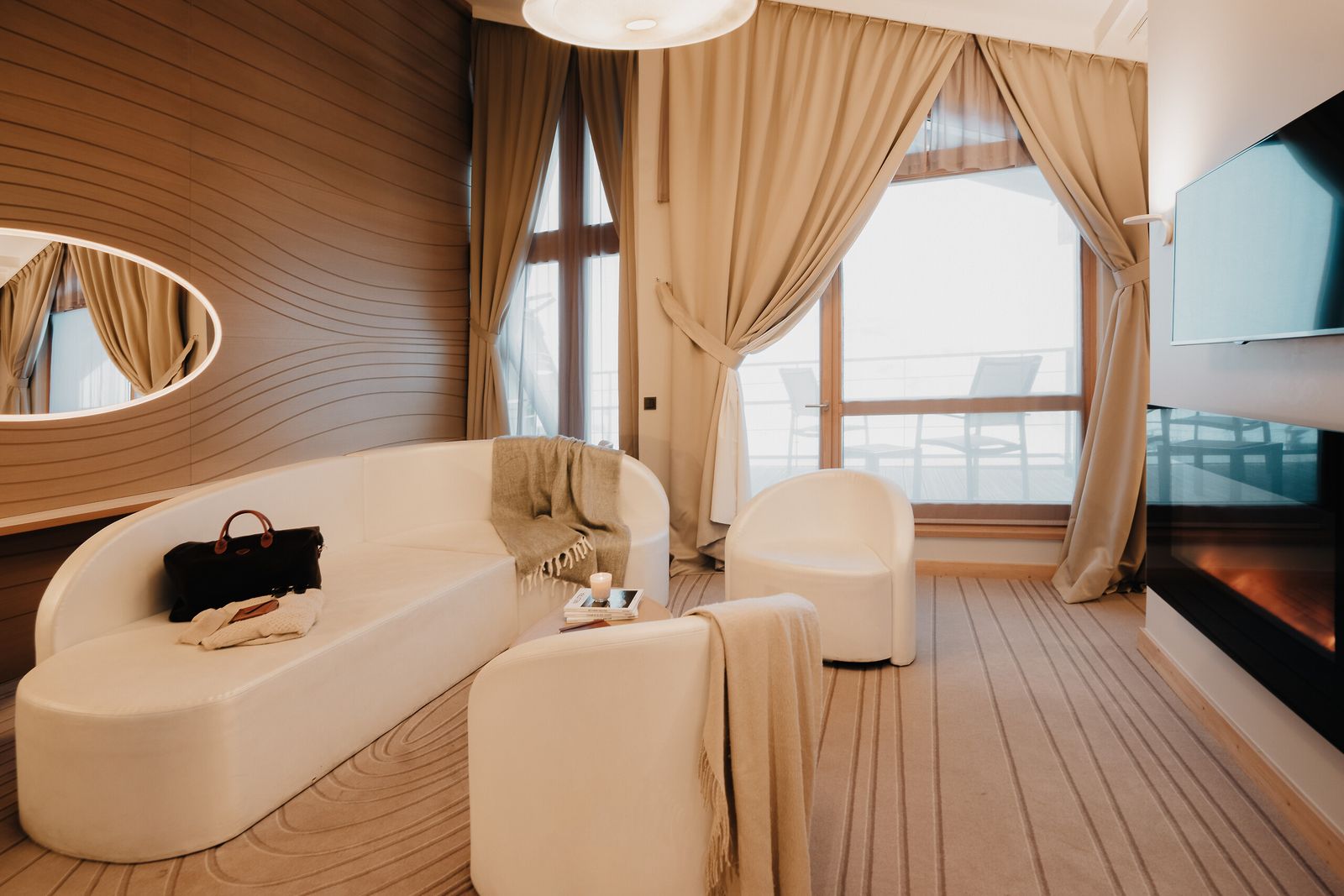 Sala de suíte com sofás brancos, piso de madeira e janela para a neve