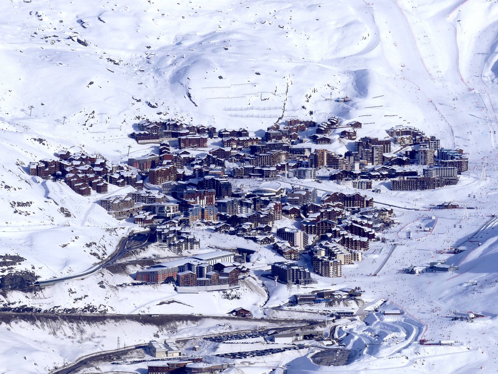 Prédios de madeira e pedra em volta da praça de neve de Val Thorens, com montanhas ao fundo